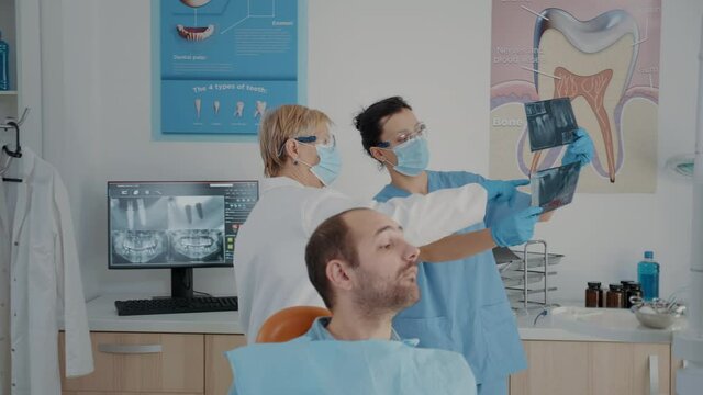 Senior dentist and nurse analyzing x ray scan to find diagnosis, looking at denture radiography results to treat patient with toothache. Dental expert and assistant doing ral care examination
