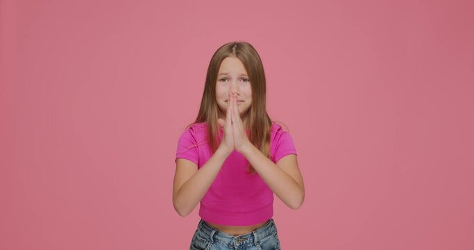 Cute child girl folding hands together, begging buy something, need help, asking please on pink studio background
