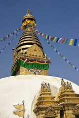 The gold spire and all-seeing eyes of Buddha atop a white-domed stupa festooned in prayer flags, Swayambhunath Buddhist temple, Kathmandu, Kathmandu Valley, Nepal