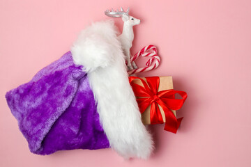 Christmas concept with candy canes, a box with a bow and a figurine of a white deer in a santa hat on a pink background. Flat lay, top view.