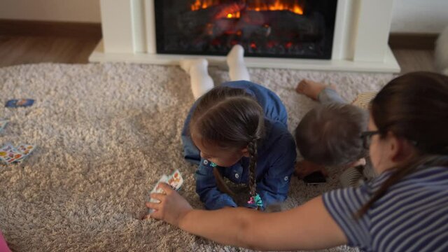 Childhood, education, isolation. Relaxing resting at home. Three little smart preschool children playing cards on carpet floor fireplace. Kids brother sister friends have interest in gambling games