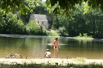 Two kids (twins) playing together in the dordogne river side in front of a fairytale house and some green trees.