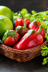 Some fresh red chili pepper and lemons in a basket with fresh coriander on a black wooden table