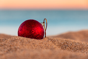 Close up front view of a red christmas decoration's ball standing on the beach of Poetto and sea in...