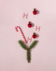 Hohoho Christmas cocktail. Candy cane, red bauble and Xmas tree branch on pastel light pink...