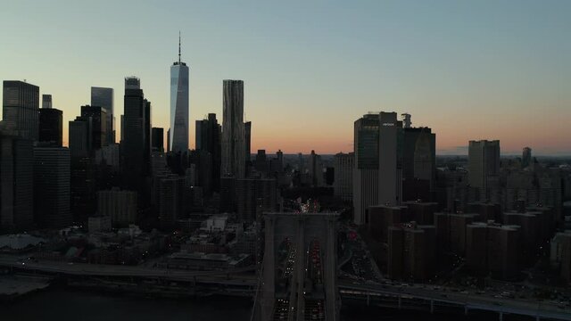 Aerial view of Brooklyn Bridge and heavy traffic on road. Flow on car lights. Silhouette of downtown skyscrapers against colourful twilight sky. Manhattan, New York City, USA