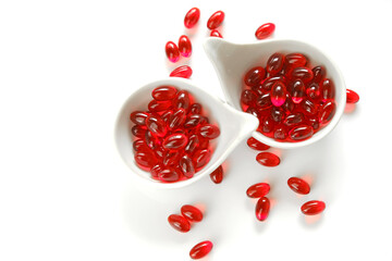 Krill oil red gelatin capsules in white ceramic cups set on a white background.omega fatty...