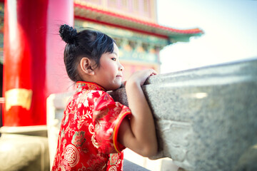 Cute little Chinese girl in cheongsam dress smiling and laughing happily in the beautiful Chinese temple background on Chinese New Year celebration