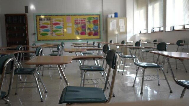 Desks in empty dark high, middle, or elementary school classroom with light coming through windows.