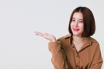 Studio cutout shot of Asian young pretty short hair female model in long brown coat jacket stand smile crossed arm hold thumb up pointing presenting product on blank copy space on white background