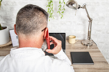Back view of middle aged man talking on the phone and working in office
