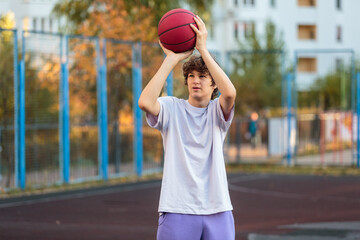 Cute teenager in white t shirt playing basketball outside. Young boy with ball learning dribble and shooting on the city court. Hobby for kids, active lifestyle