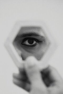 Grayscale photo of man looking at his eye in mirror