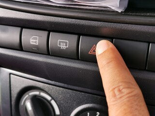 Close up view car interior. Finger pressing emergency light button on dashboard.
