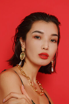 Portrait of woman with golden earring and necklace against red background