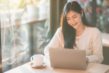 Portrait freelance business beautiful positive smile young asian woman girl wearing warm clothes online working with laptop computer with coffee cup mug at house home in the living room inside or cafe