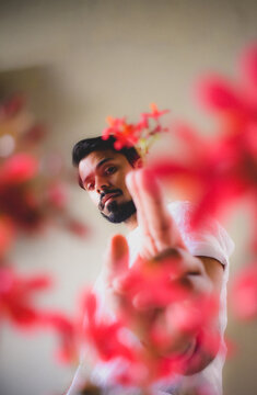 South Asian man in light shirt beside red flowers