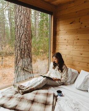 Woman in light comfy outfit sitting on bed and reading