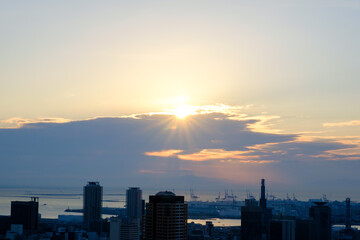 Fototapeta na wymiar 都市の夜明け。日の出の時間が過ぎるが、太陽は厚い雲に隠れていたが、ようやく雲の切れ目から顔を出す。神戸の山手ヴィーナスブリッジから撮影