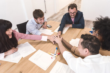 5 multiethnic people in an office sitting putting their hands together in the center of the table