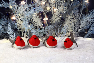 Felt toy bullfinches sit on artificial snow and artificial blue and white trees stand behind them...