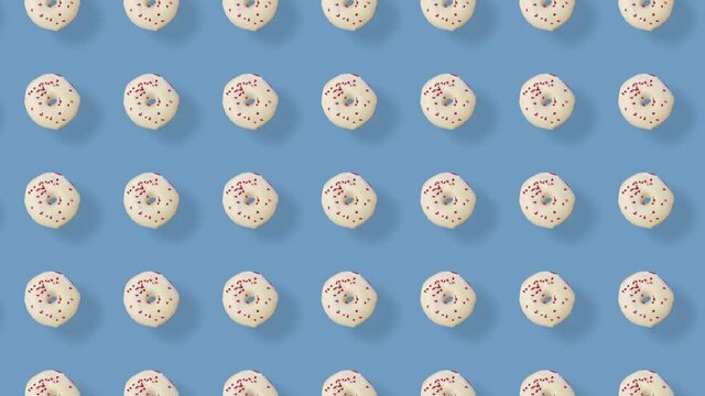 Colorful pattern of donuts isolated on blue background with shadows. Seamless pattern with donut. Doughnuts. Top view. Realistic animation. 4K video motion