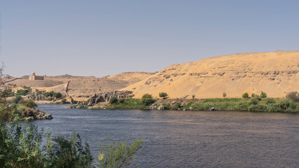 The Blue Nile flows calmly. Along the banks -green vegetation, picturesque boulders. Sand dunes against the azure sky. Egypt