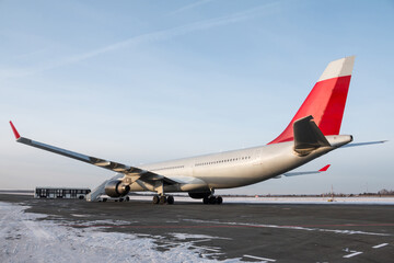 Wide body passenger airplane with boarding stairs at the winter airport apron. Shuttle bus near the aircraft