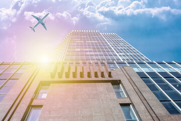 A modern office skyscraper and a white passenger airliner flying over this building