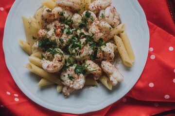 shrimp scampi atop penne pasta in white bowl with red and white polka dot cloth