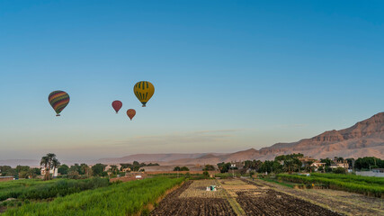 Bright balloons fly over the cultivated fields of the Nile Valley. Plowed soil, sugar cane plantations are visible. Picturesque mountains, sand dunes against the sky. Egypt. Luxor