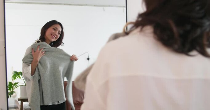 Young beautiful Asian woman holding a Shirt in front of the mirror happy girl at home trying on clothes in the mirror before going out People's daily routine  at home  