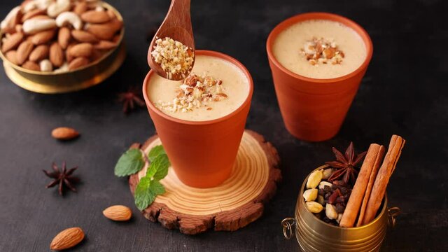 Kesar Badam milk shake Almond Saffron milk woman hand serving smoothie 4K video footage Kerala India. Kheer or North Indian traditional health drink in clay pot Flavoured milk badam lassi dry fruit