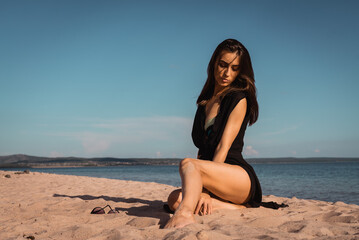Fototapeta na wymiar a young woman in a black dress lies on the sand. High quality photo