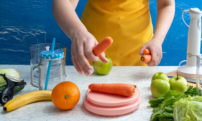 Woman's hand picks up carrots from scales after weighing. There are other smoothie ingredients on table. Selective focus. Healthy eating.