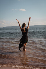 Obraz premium A young woman in a black dress stands in the water by the sea. High quality photo