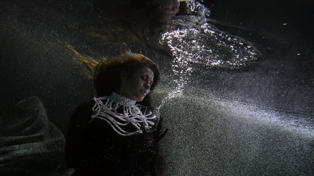 romantic portrait of lady underwater, elegant woman in black medieval dress is holding glass goblet