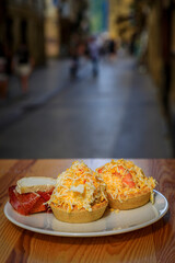 Traditional pintxos of Russian salad and Serrano iberico ham tostada on an outdoor table at a bar...
