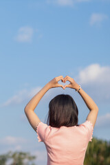 A woman raises her hand above her head to make a heart symbol on the background of the bright...