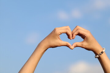 A woman raises her hand above her head to make a heart symbol on the background of the bright...