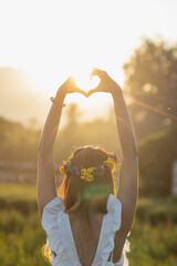 A woman raises her hand above her head to make a heart symbol on the background of the bright...