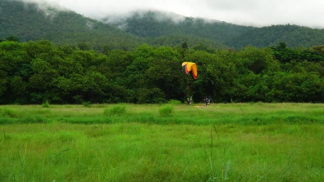 An athlete on a paramotor gliding and flying to landing on the runway with another paramotor pass over, Have green forest are background, Paramotor gliding is an extreme sport.