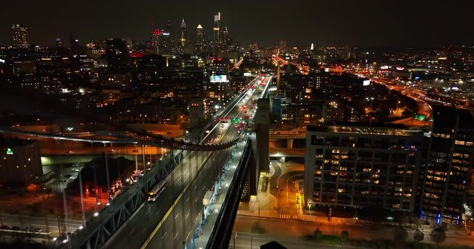 Urban American city skyline. Suspension bridge at night. Aerial flight passes by. Dramatic cinematic shot.