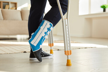 Close up leg of man walking with crutches in ankle brace with support adjustable strap fracture...