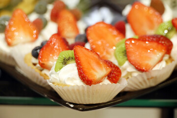 Creamy cakes with fresh fruits and berries, selective focus. Sweet cream dessert with strawberry, kiwi and blueberries