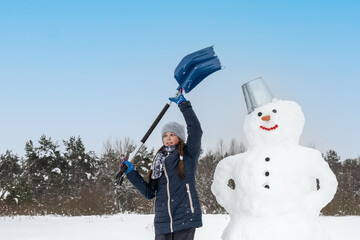 teenage girl makes a snowman and holds a shovel. The concept of active winter recreation. Family vacation