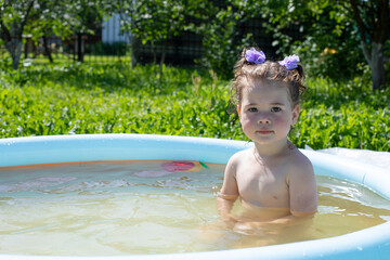 Little Caucasian girl 2 years old bathes in an inflatable pool in the garden, a girl with wet hair sits in the pool