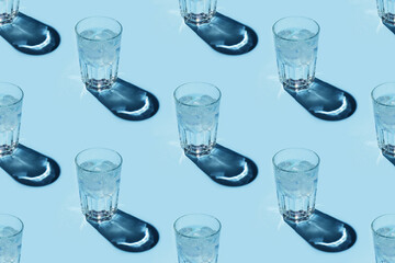 Seamless repetitive pattern with transparent glasses of water with ice cubes on blue background.