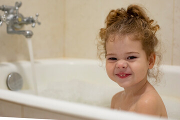 Little Caucasian girl 2 years old in the bathroom, the girl laughs and makes faces