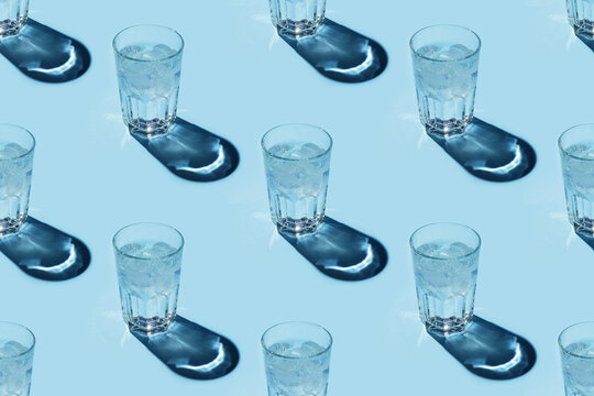 Seamless repetitive pattern with transparent glasses of water with ice cubes on blue background.